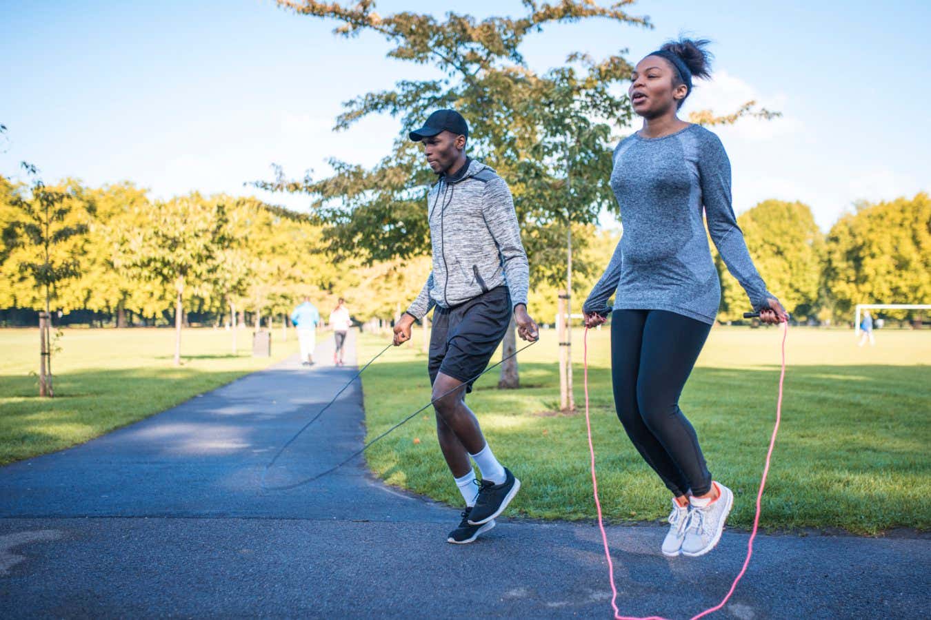 Two friends exercising outdoors in a park on a sunny day. They are jumping with jumping rope.